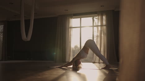 A-young-woman-in-white-sportswear-is-stretching-with-a-large-hall-with-large-windows-in-a-slow-motion-scheme-the-sun's-rays-shine-through-the-window.-Healthy-lifestyle-healthy-morning
